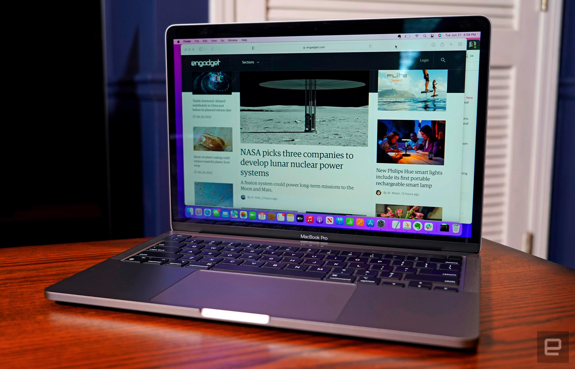 The MacBook Pro 13-inch M2 (2024) sits open on a wooden dining room tabletop in a room with blue walls and white doors.
